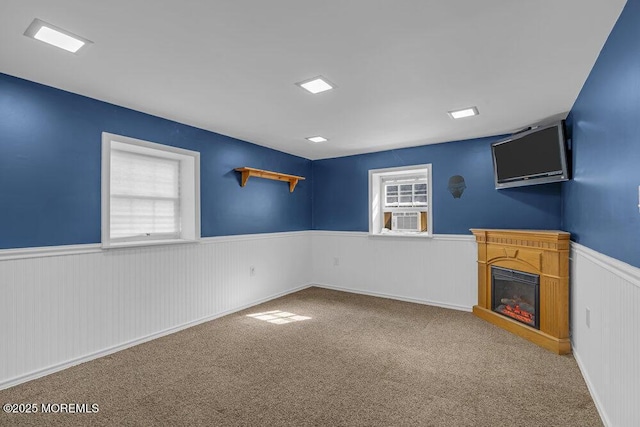 interior space featuring a glass covered fireplace, a wainscoted wall, and carpet flooring