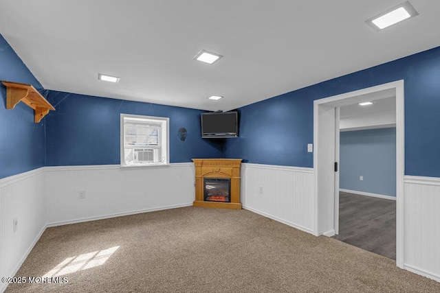 unfurnished living room featuring wainscoting, carpet, a glass covered fireplace, and cooling unit