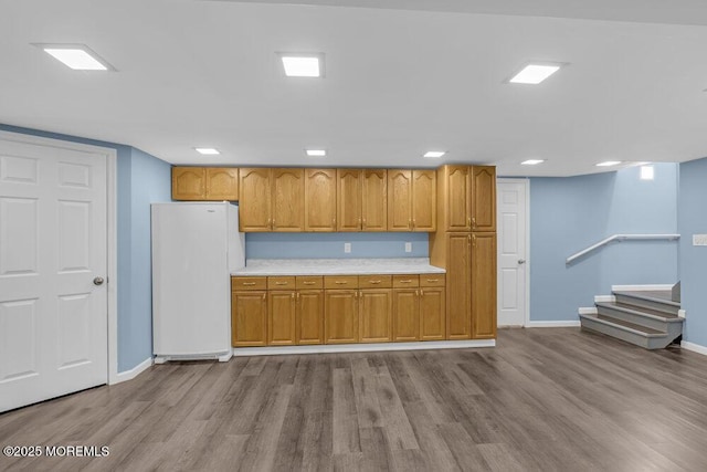 kitchen with wood finished floors, baseboards, light countertops, freestanding refrigerator, and brown cabinetry