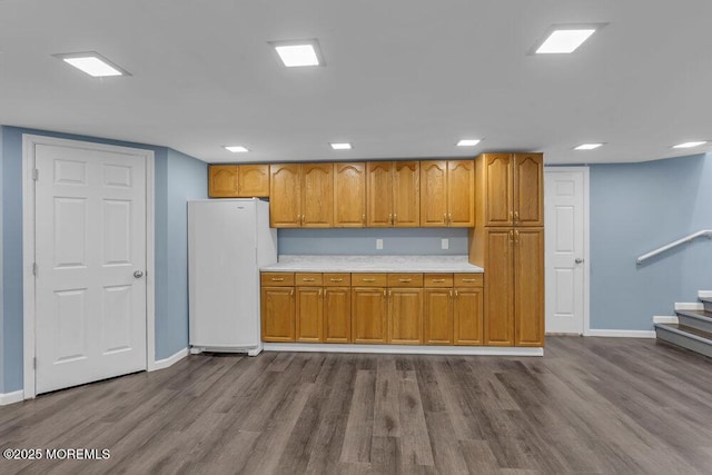 kitchen with baseboards, dark wood finished floors, brown cabinetry, freestanding refrigerator, and light countertops