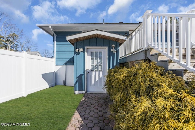 view of exterior entry featuring a lawn and fence