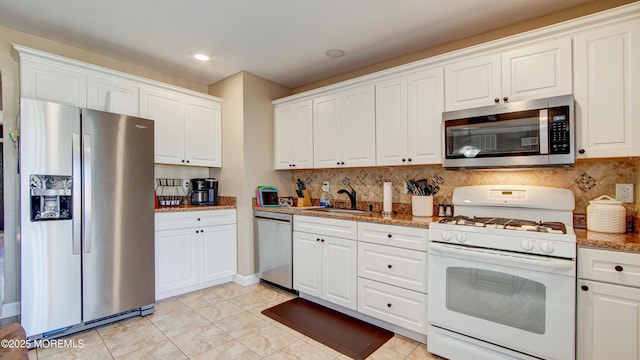 kitchen with backsplash, appliances with stainless steel finishes, white cabinets, a sink, and light stone countertops