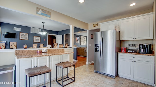 kitchen with stainless steel fridge, white cabinetry, a breakfast bar area, and decorative light fixtures