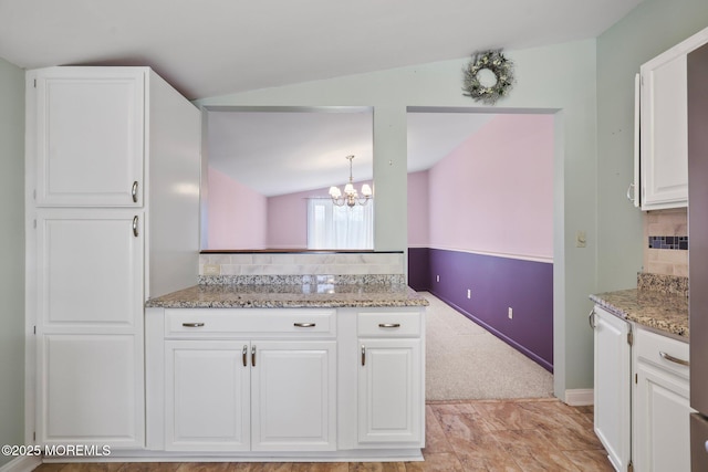 kitchen with light stone counters, white cabinets, vaulted ceiling, decorative backsplash, and an inviting chandelier