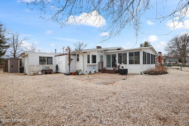 back of house featuring a sunroom, a chimney, an outbuilding, a patio area, and a shed