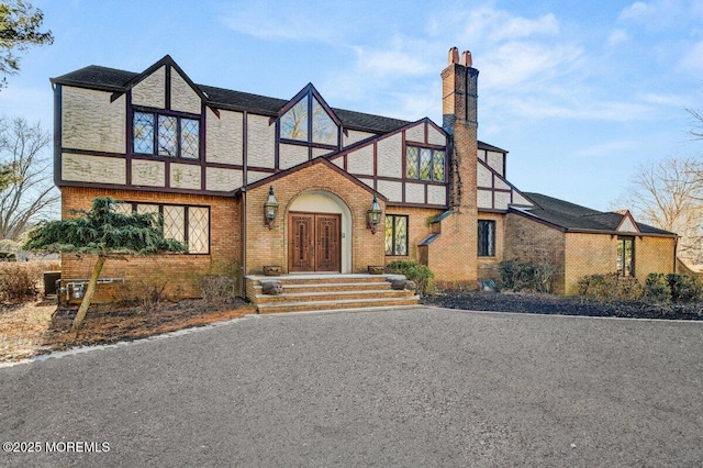 english style home with brick siding, a chimney, and french doors