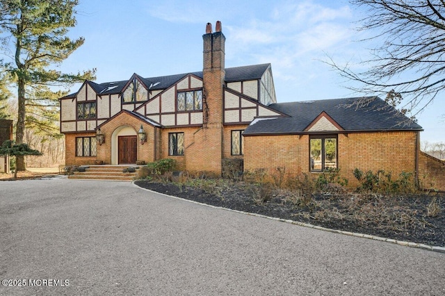 view of front facade featuring roof with shingles, a chimney, and brick siding