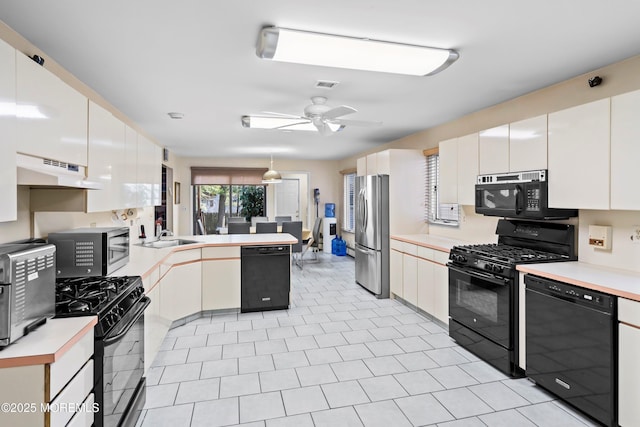 kitchen with under cabinet range hood, a peninsula, black appliances, and light countertops