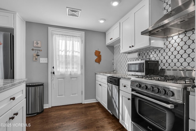 kitchen with light stone counters, stainless steel appliances, dark wood-style flooring, wall chimney exhaust hood, and tasteful backsplash