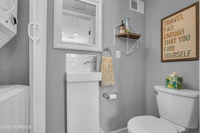 half bath with stacked washer / drying machine, visible vents, a sink, and toilet