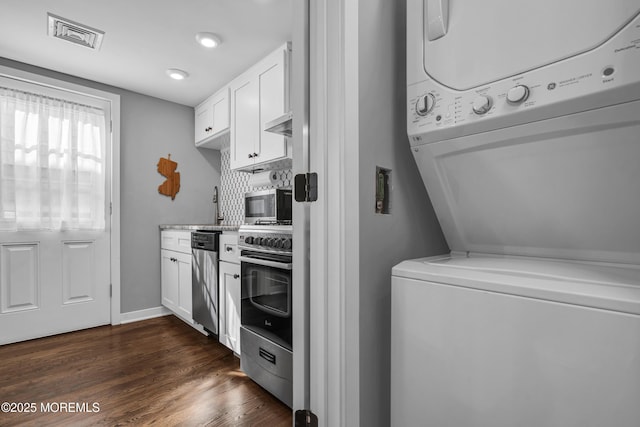 laundry room featuring laundry area, visible vents, dark wood finished floors, stacked washer / drying machine, and a sink