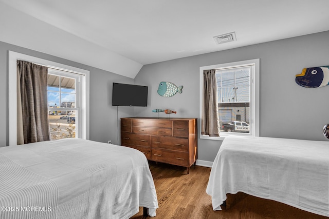 bedroom with baseboards, visible vents, vaulted ceiling, and wood finished floors