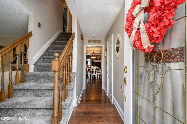 foyer with dark wood-type flooring, stairway, a textured ceiling, and baseboards