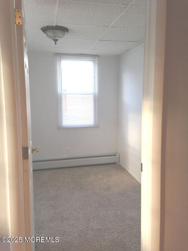 empty room featuring carpet floors, a baseboard radiator, and a paneled ceiling