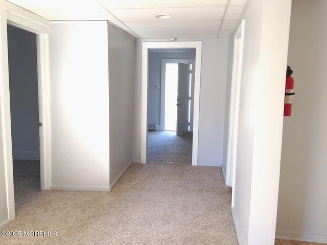 hallway featuring a paneled ceiling, baseboards, and carpet flooring