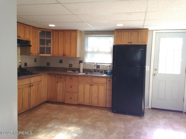 kitchen with brown cabinets, glass insert cabinets, a sink, under cabinet range hood, and black appliances