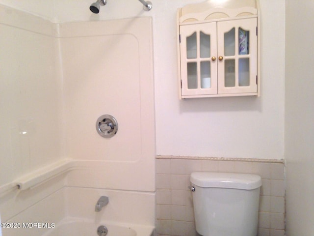 bathroom featuring toilet, wainscoting, tile walls, and bathing tub / shower combination