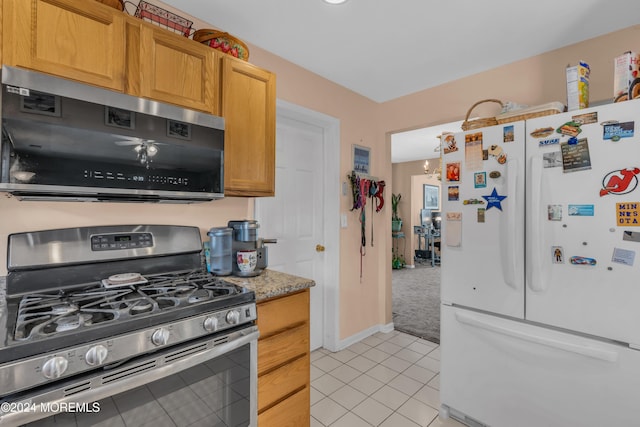 kitchen with light tile patterned floors, stainless steel range with gas stovetop, freestanding refrigerator, and baseboards