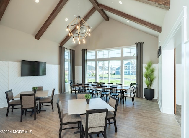 dining area featuring a chandelier, high vaulted ceiling, light wood-style flooring, a wainscoted wall, and a wealth of natural light