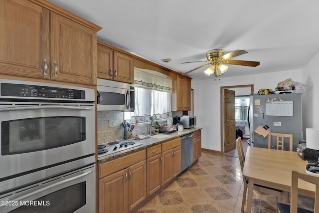 kitchen with a sink, baseboards, appliances with stainless steel finishes, decorative backsplash, and brown cabinetry