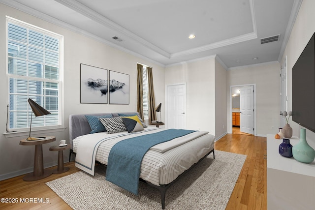 bedroom featuring wood finished floors, visible vents, baseboards, ornamental molding, and a raised ceiling