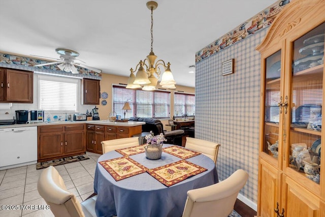 dining area featuring a healthy amount of sunlight, light tile patterned floors, wallpapered walls, and ceiling fan with notable chandelier