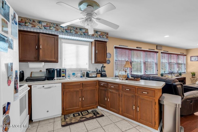 kitchen with a peninsula, white appliances, open floor plan, light countertops, and backsplash