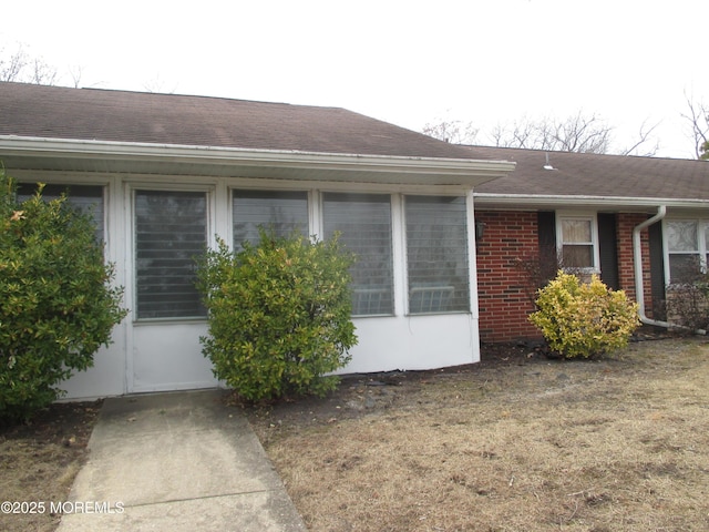 view of side of property featuring a yard, brick siding, and roof with shingles