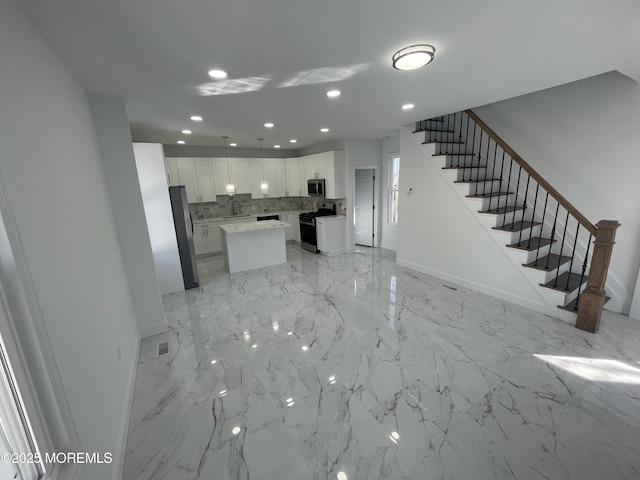 kitchen featuring baseboards, white cabinets, a center island, stainless steel appliances, and backsplash