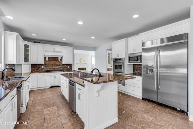 kitchen with white cabinetry, a sink, an island with sink, and built in appliances