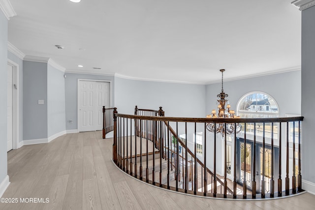 hallway featuring light wood finished floors, ornamental molding, an upstairs landing, a chandelier, and baseboards