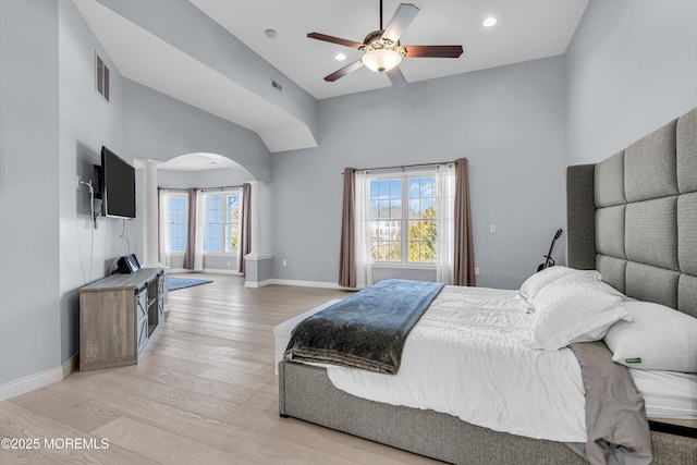 bedroom with light wood-type flooring, arched walkways, visible vents, and baseboards