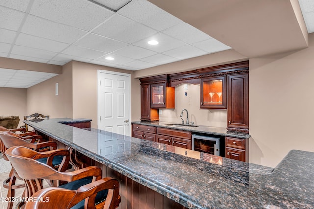 kitchen with beverage cooler, dark stone counters, a breakfast bar, and a sink