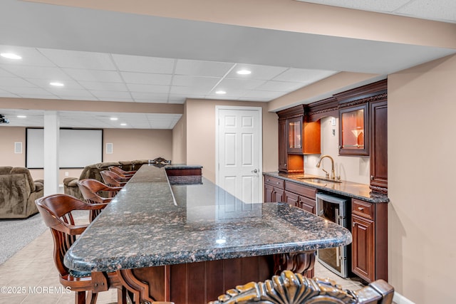 kitchen with a breakfast bar, wine cooler, glass insert cabinets, open floor plan, and a sink