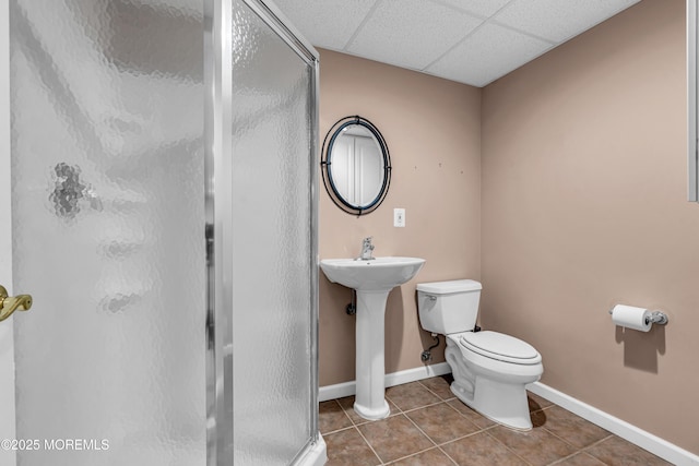 bathroom featuring a stall shower, baseboards, a drop ceiling, toilet, and tile patterned flooring