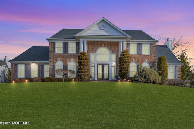 greek revival inspired property with french doors, brick siding, and a front lawn