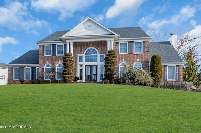 neoclassical home with a front yard, a chimney, french doors, and brick siding