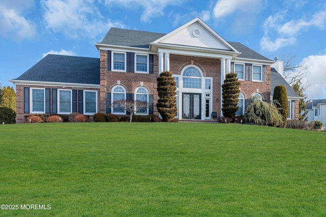 neoclassical / greek revival house with a shingled roof, french doors, brick siding, and a front lawn