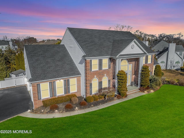 view of front facade featuring aphalt driveway, brick siding, roof with shingles, a front yard, and a gate