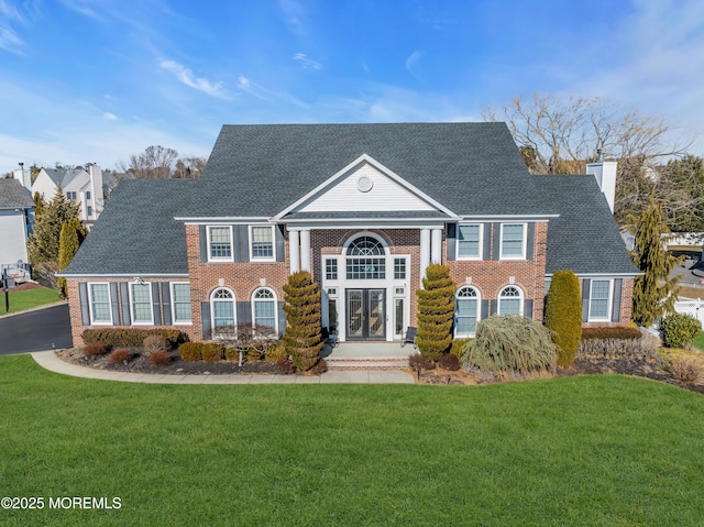 neoclassical home with brick siding, a chimney, a front lawn, and roof with shingles