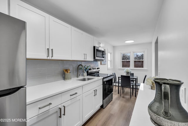 kitchen with a sink, stainless steel appliances, light countertops, and white cabinets