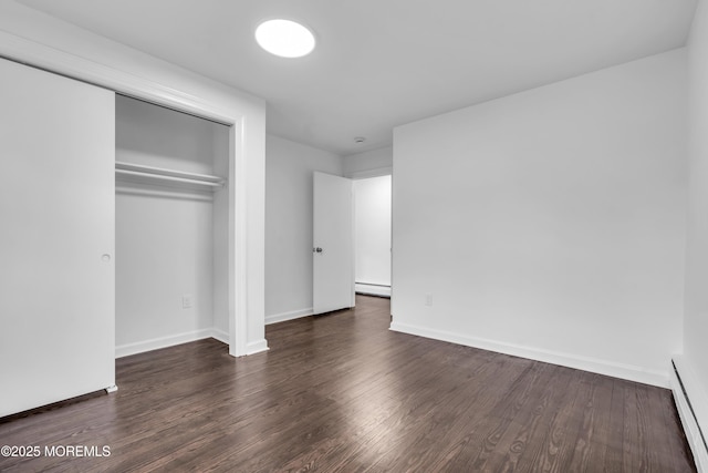 unfurnished bedroom featuring a closet, baseboards, baseboard heating, and dark wood-style flooring