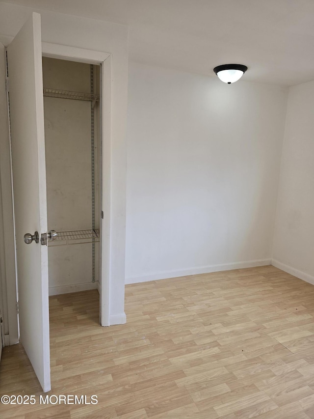 unfurnished bedroom featuring light wood-style floors, baseboards, and a closet