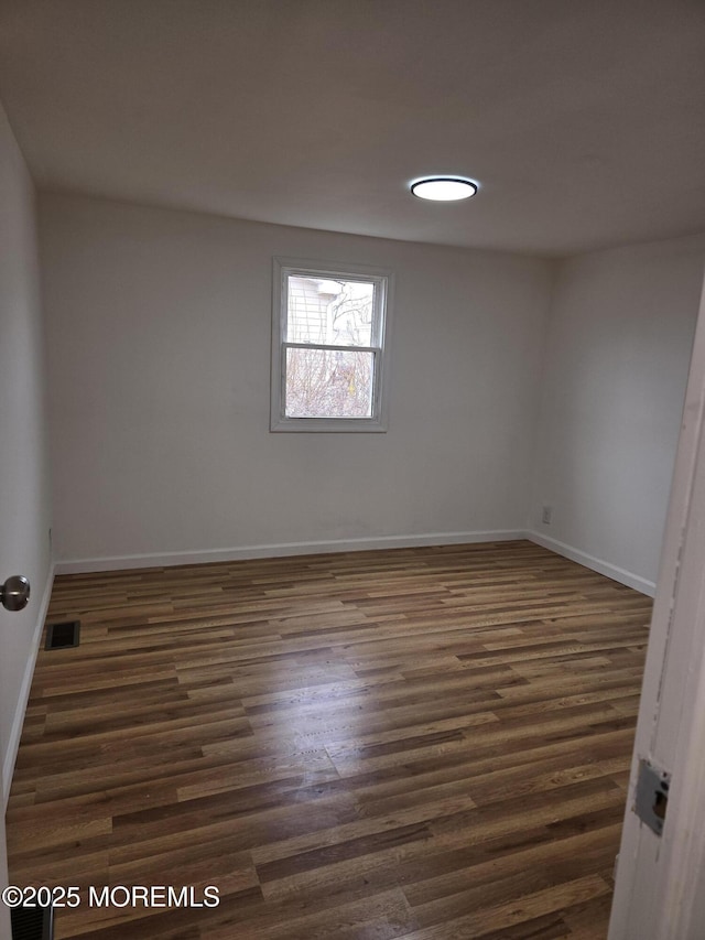 spare room with dark wood-type flooring, visible vents, and baseboards