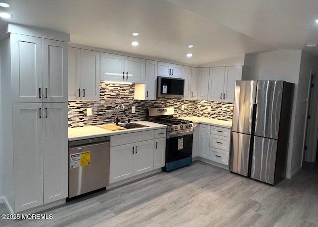 kitchen with stainless steel appliances, a sink, light countertops, light wood-type flooring, and backsplash