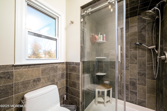 bathroom featuring a wainscoted wall, a shower stall, toilet, and tile walls