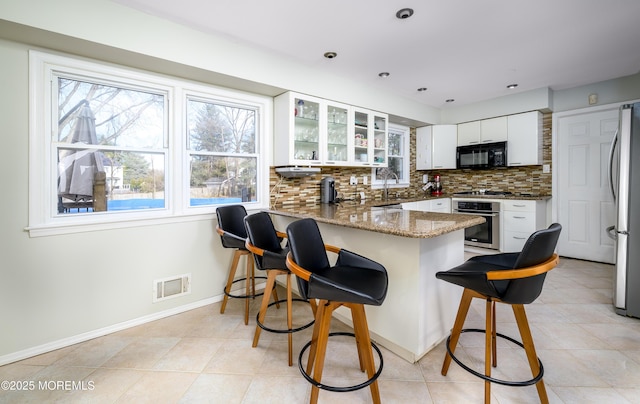 kitchen featuring stainless steel appliances, visible vents, backsplash, white cabinets, and a peninsula