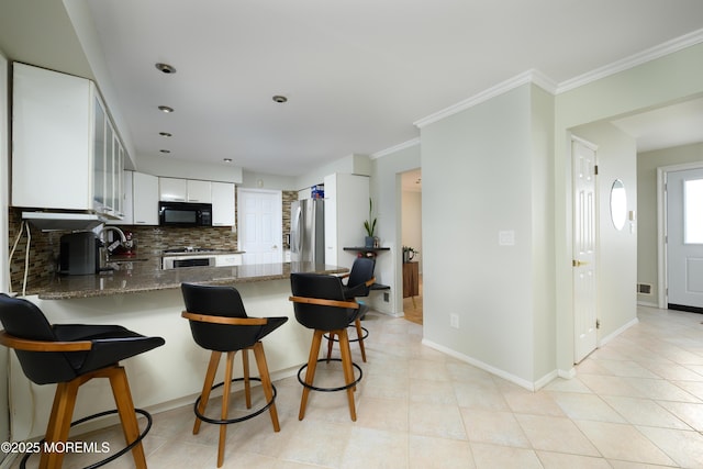 kitchen featuring crown molding, backsplash, appliances with stainless steel finishes, dark stone counters, and a peninsula