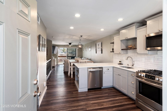 kitchen featuring a peninsula, stainless steel appliances, light countertops, open shelves, and a sink