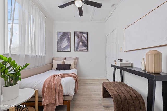 bedroom with crown molding, light wood-style flooring, attic access, a ceiling fan, and baseboards